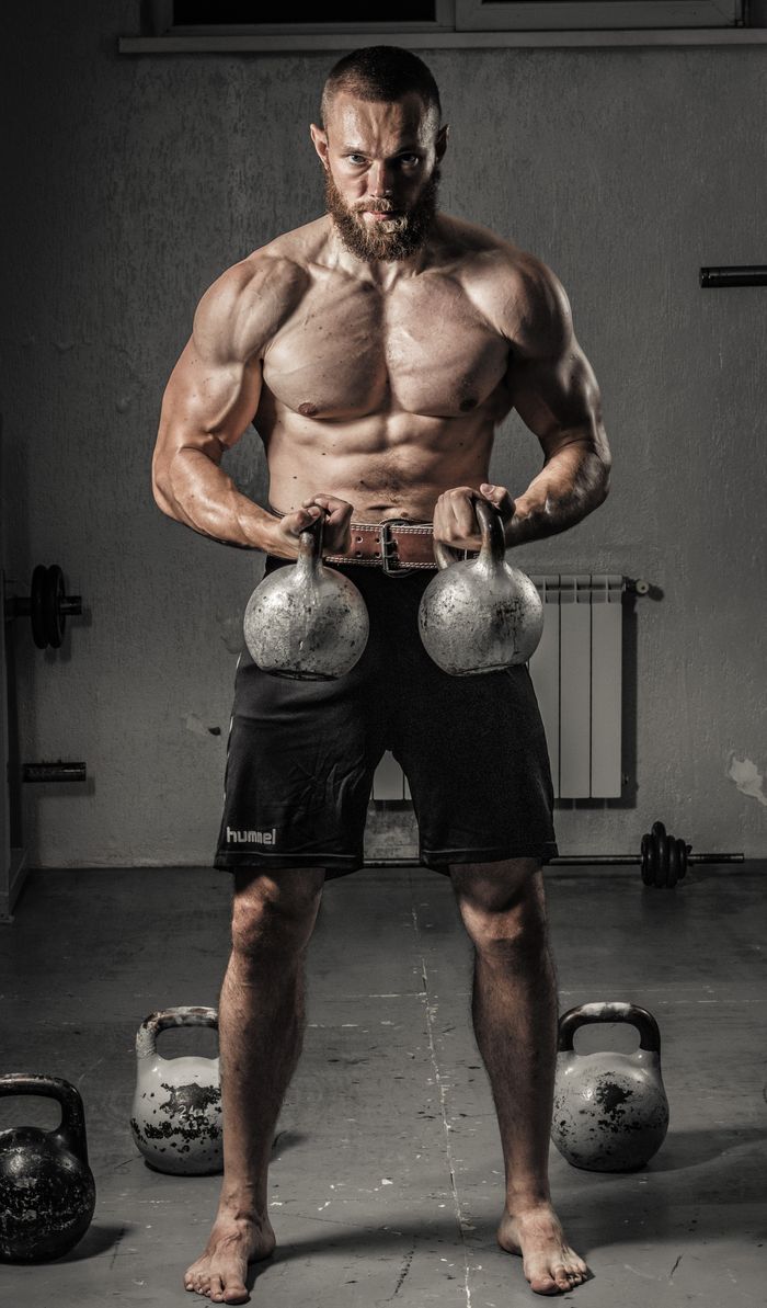 About Shirtless man with muscular build lifting kettlebells indoors, showcasing strength and fitness.